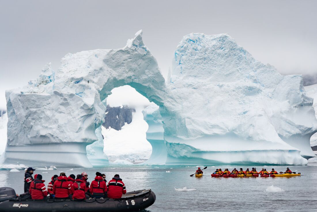 Zodiacs and kayaks marvel at an arched iceberg off the coast of Antarctica