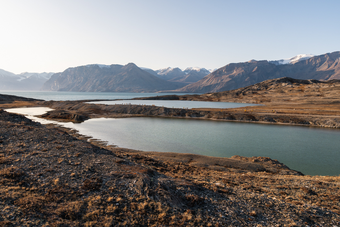 Distant travellers walk along a spit through a fjord in Ella Island landscape northeastern Greenland
