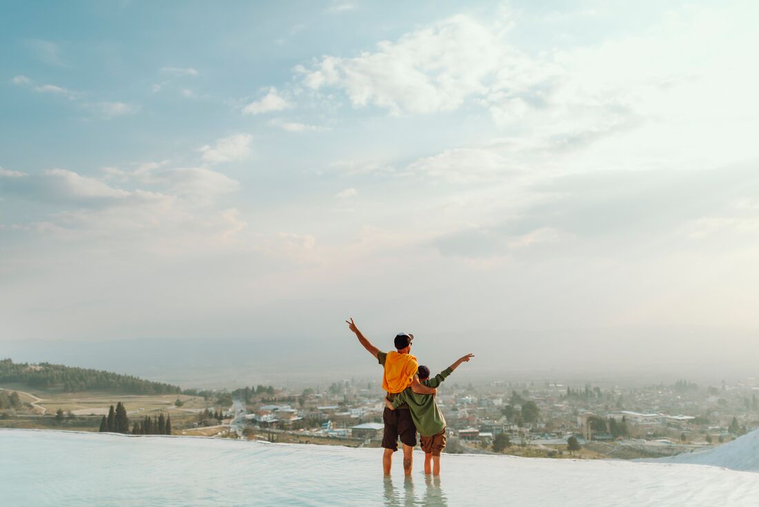 Intrepid traveller father and son throw up their hands in joy on the edge of the TUrkish landscape in Pamukkale pools