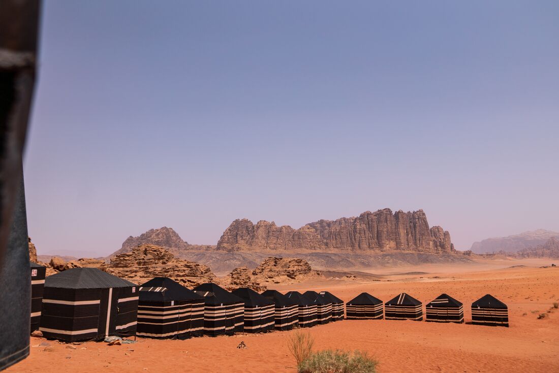 Square black tents with gold bands arrayed further from the camera in the desert of Wadi Rum in Jordan