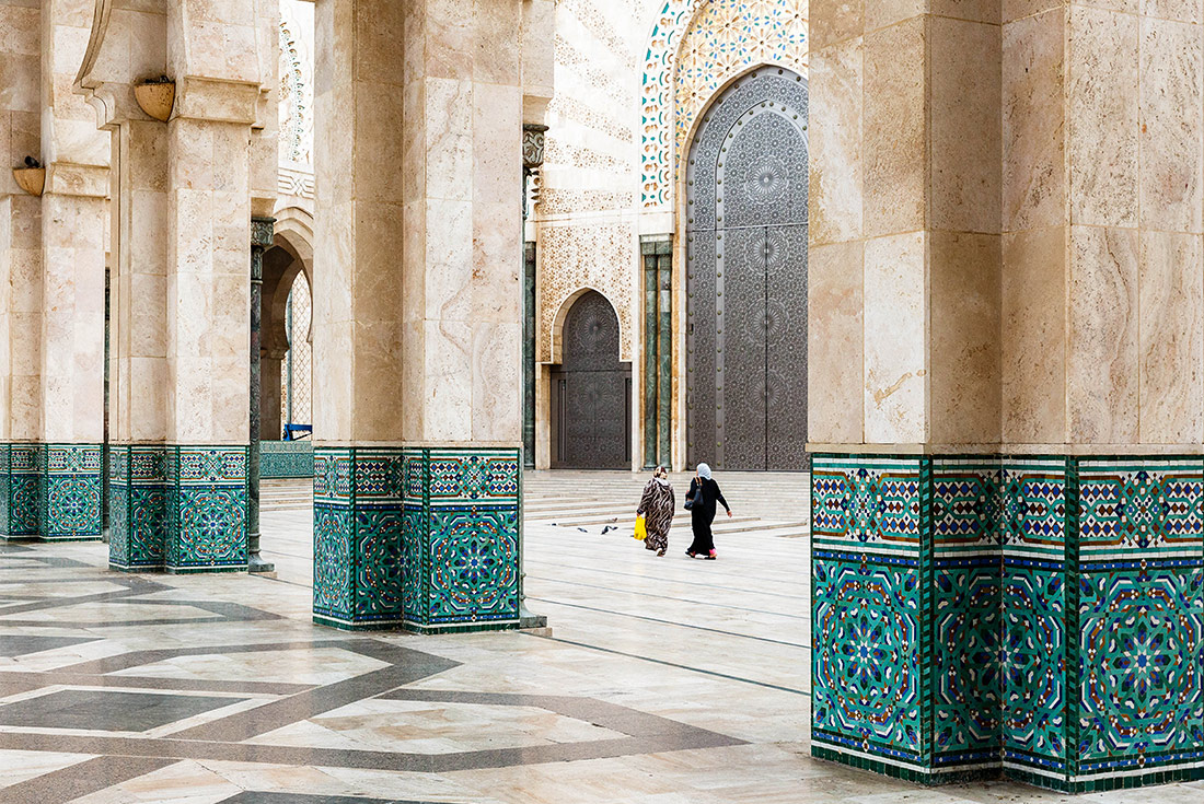 Local women walking through archways of Hassan II Mosque, Casablanca, Morocco