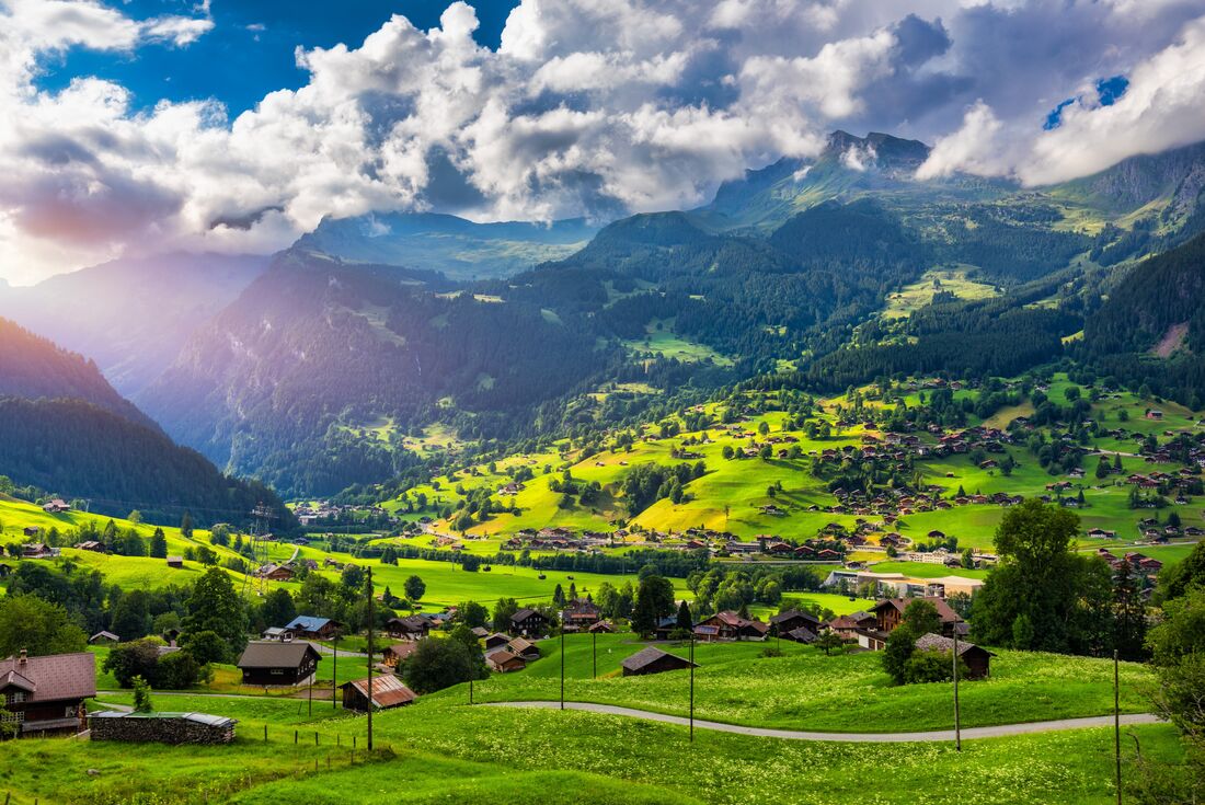 Sun sprays across Grindelwald village sprawling across bright green valley in the mountains of the Swiss Alps