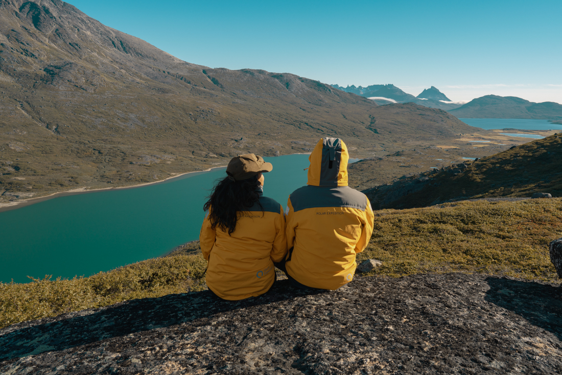 Travellers in yellow cold weather coats sit on a rocky outcrop looking out over Lindenow Fjord in Greenland