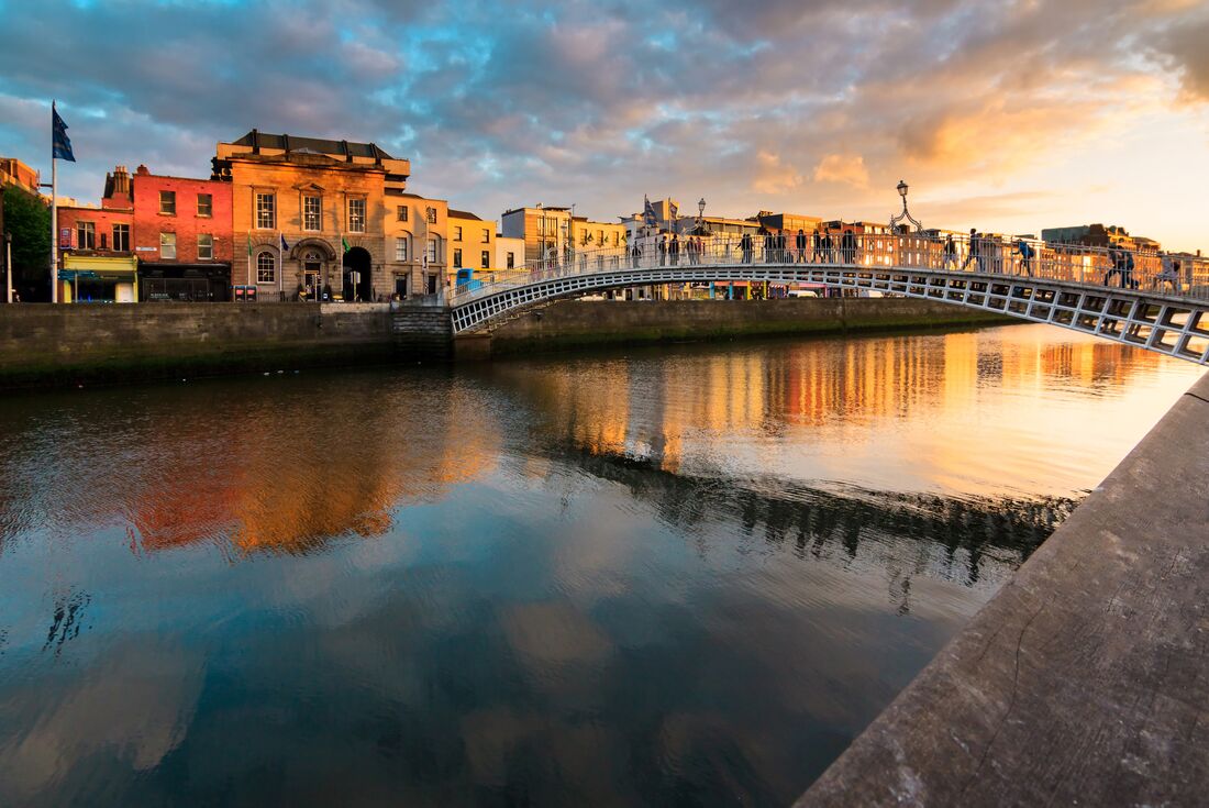 People walking over water on the Hapenny Bridge at a colourful sunset in Dublin, Ireland