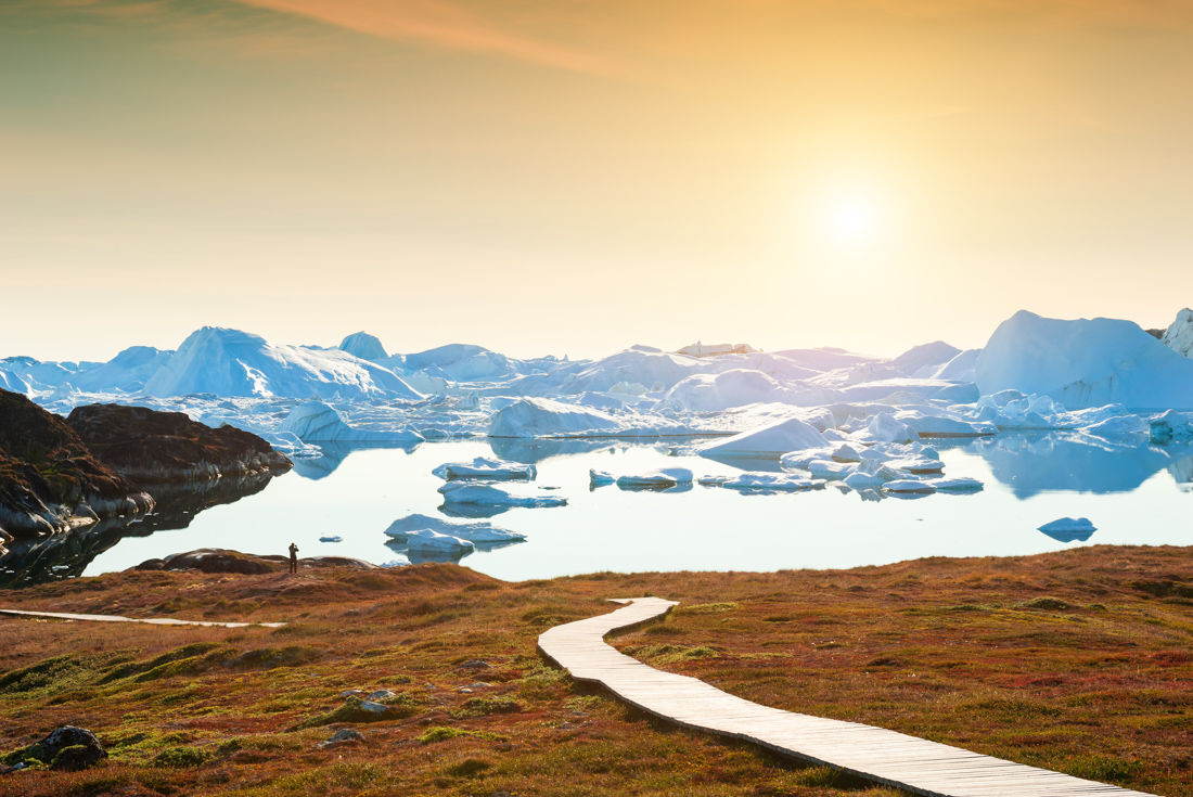 Traveller marvels and takes a photo at sunset on Disko Bay looking ta the Ilulissat Fjord on a trai in Greenland