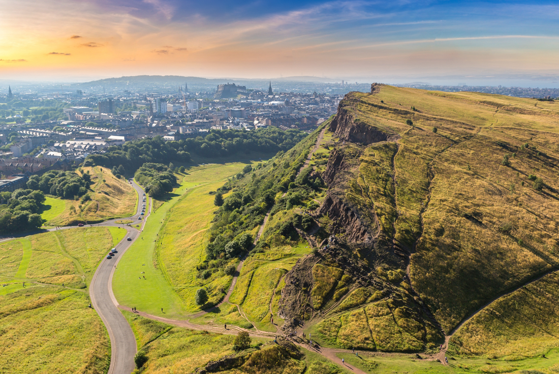View of Edinburgh from Arthur's Seat top, with travellers climbing Salisbury Crags in the foreground