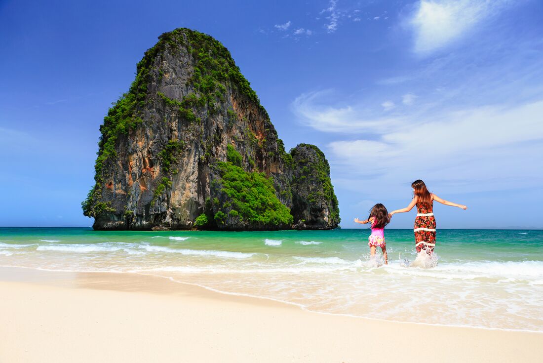Mother and daughter laugh with joy run into the surf at Railay beach in Krabi Thailand