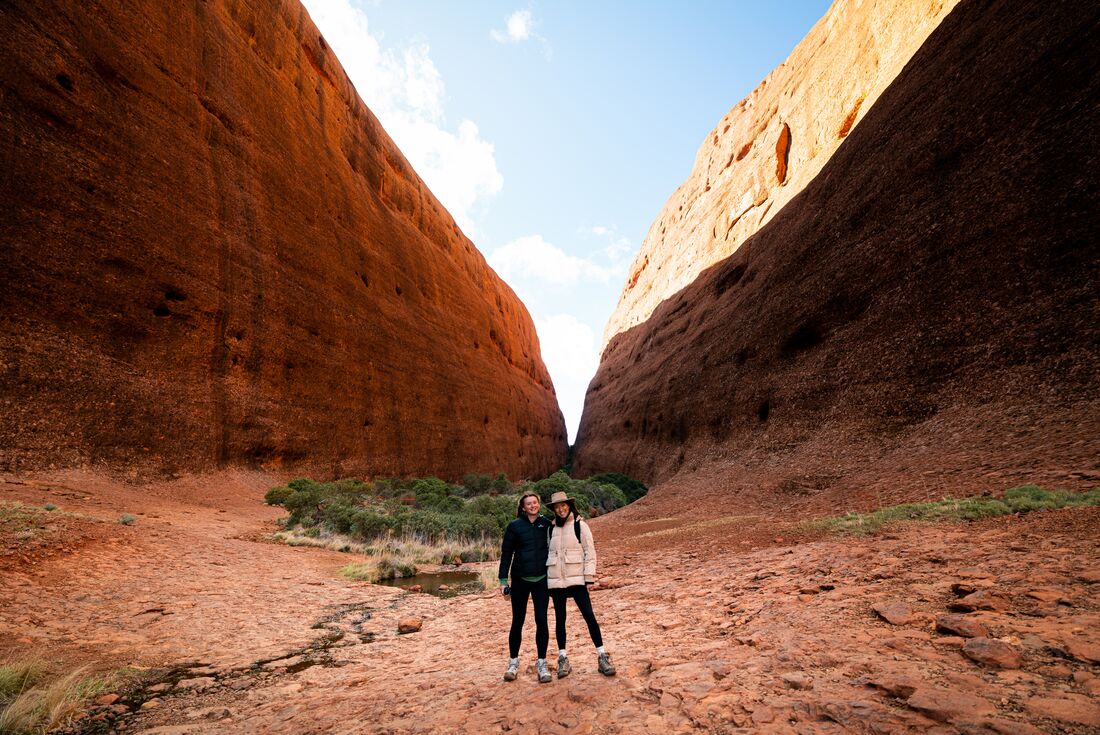 Two travellers pose happily between sweeping stone sides of Kata Tjuta in the Red Centre of Australia