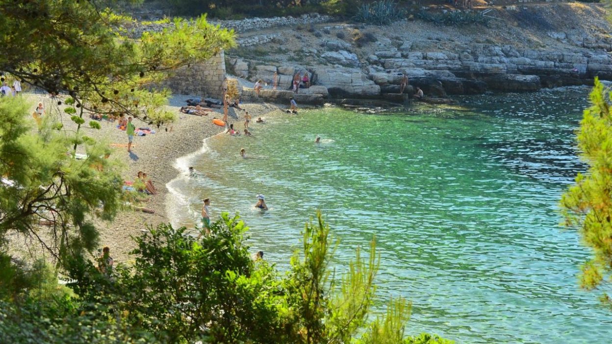 A few people are spread out along the ocean on a beachfront on Vis Island in Croatia.