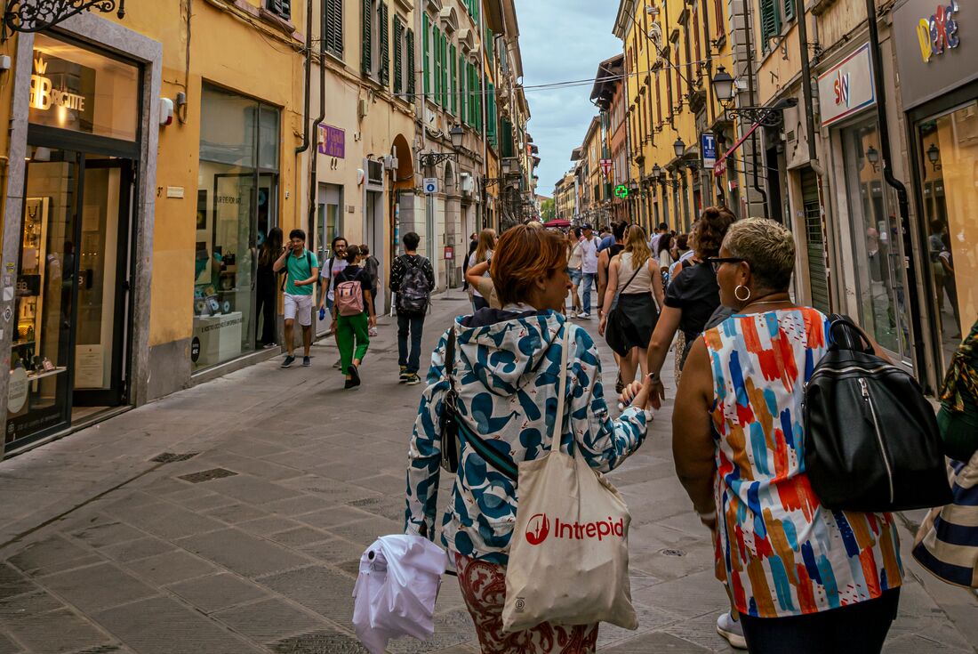Leader and traveller chatting while on a walk on streets lined with shops in Pisa, Italy