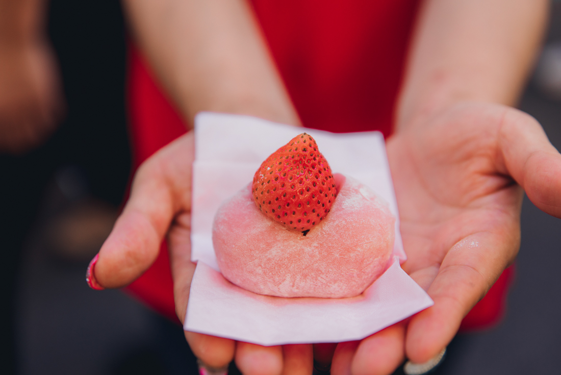 A frosted gelatinous ball dessert topped with a strawberry held in traveller's hands in Tokyo food markets