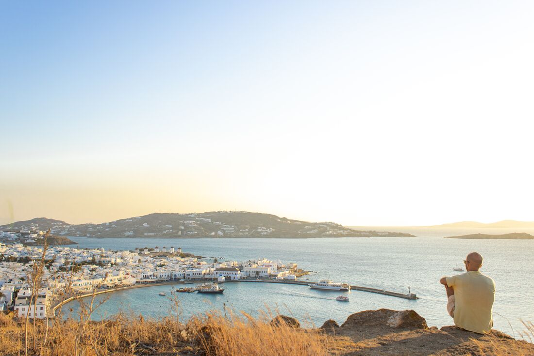 Traveller perched on a high hill looks out over the sparkling Aegean and the island of Mykonos