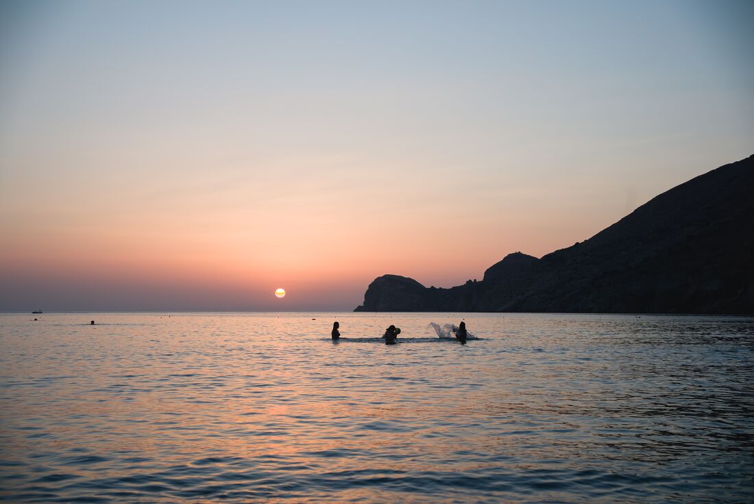 Intrepid travellers swimming and splashing in Syros at sunset