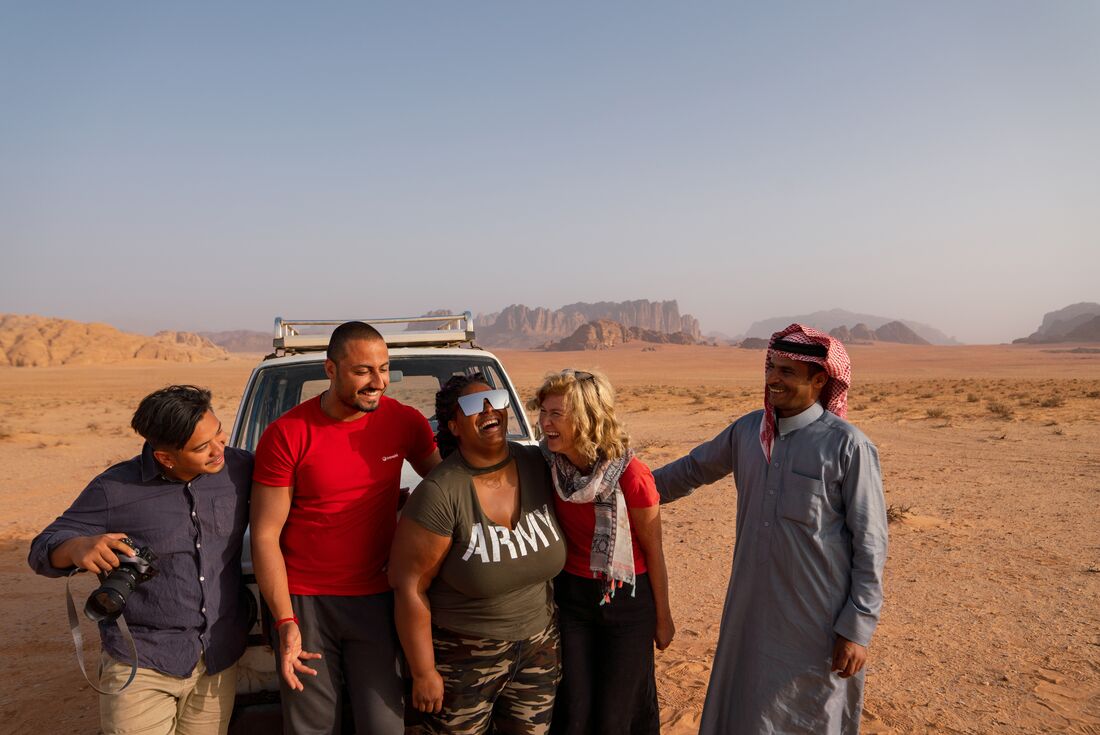 Travellers laugh with leader and local guide waiting for sunset in Wadi Rum on a 4x4 vehicle