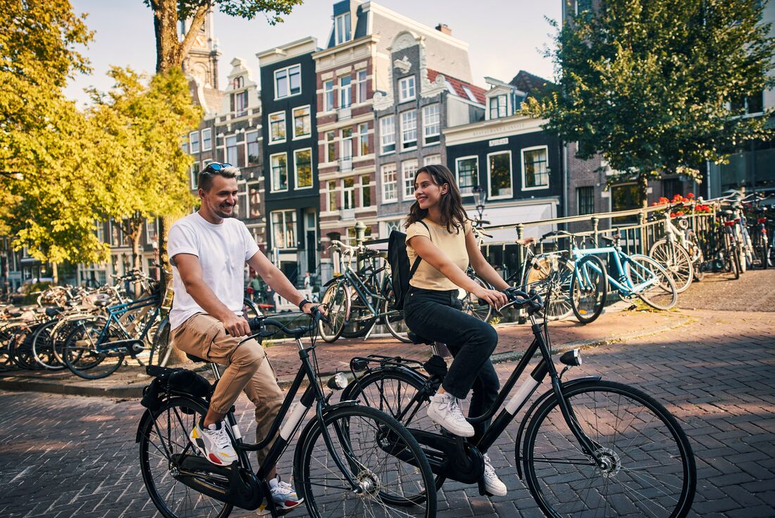 Intrepid traveller couple cycling through the streets of Amsterdam, Netherlands