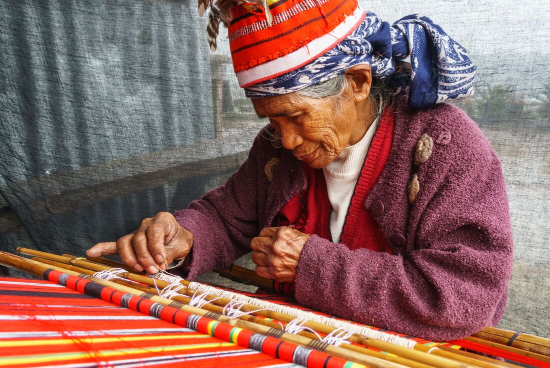 Elderly Ifugao woman weaving with loom in traditional clothes and hat