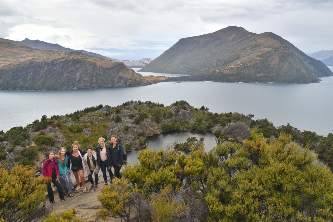 Group of travellers standing on a hill with the beautiful Lake Wanaka in the background in Wanaka, South Island, New Zealand